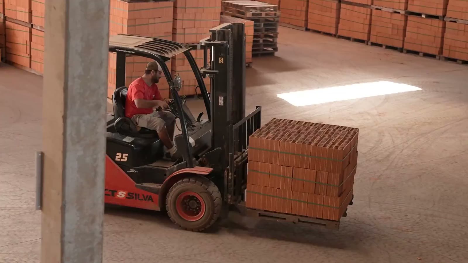 Empilhadeira levando um palete de tijolos dentro do galpão
